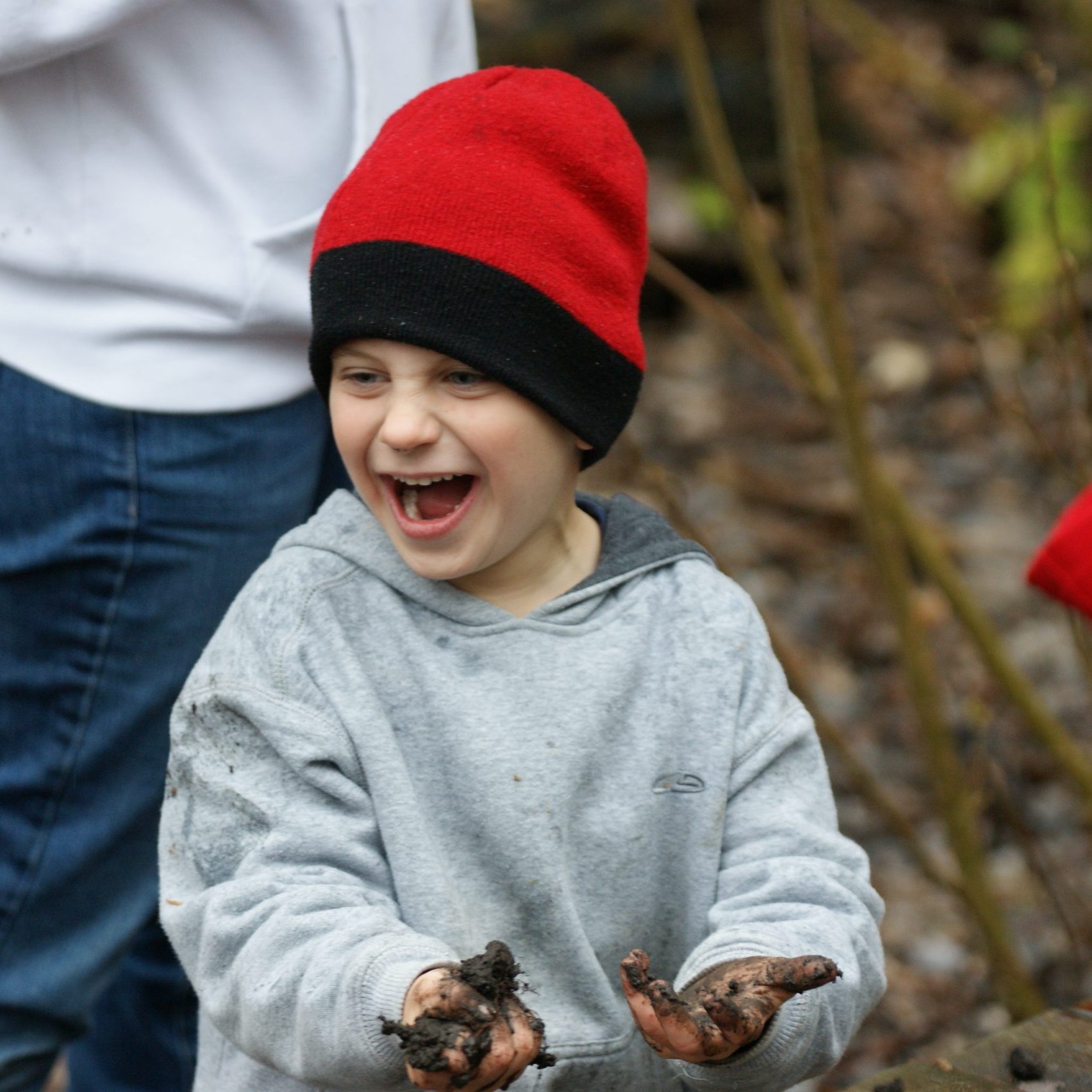 Young boy wearing red hat smiling with dirt in his hands